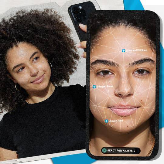 Een persoon met krullend haar in een zwart shirt houdt een telefoon vast tegen een kleurrijke achtergrond.