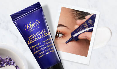 Alt text: A tube of Kiehl's Midnight Recovery Eye cream beside a close-up of a woman's eye as she applies the product. The tube is dark blue with gold text, highlighting its restorative properties for youthful-looking eyes.