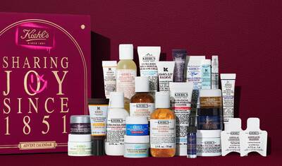 Kiehl's Adventkalender geschenkdoos in dieprood met gouden tekst, getoond naast 24 mini huidverzorgingsproducten, waaronder Ultra Facial Cream, Calendula Toner, Retinol Serum en Lip Balm #1. Een roze spuitverf-afbeelding aan de zijkant benadrukt de waarde van de set.