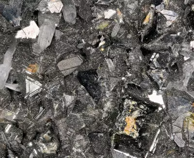 Close-up of a cluster of shiny, dark crystals with a textured, glittery surface, showcasing various crystal shapes and formations.