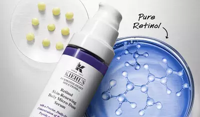 A close-up of Kiehl's Retinol Skin-Renewing Daily Micro-Dose Serum bottle next to a petri dish showcasing round capsules and molecular structures, emphasizing the product's pure retinol content.