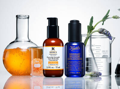 Two Kiehl's skincare products, a line-reducing concentrate and a recovery concentrate, displayed with science glassware and orange liquid.