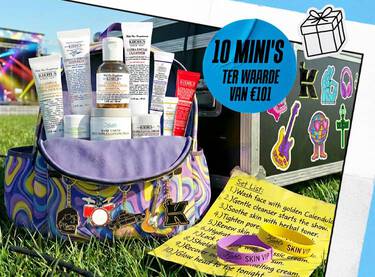 Een promotionele banner van Kiehl's in festivalthema met een kleurrijke reistas vol met 10 mini huidverzorgingsproducten, staand op het gras naast een zwarte flightcase met stickers. Een gele 'Set List' en festivalbandjes liggen op de voorgrond.