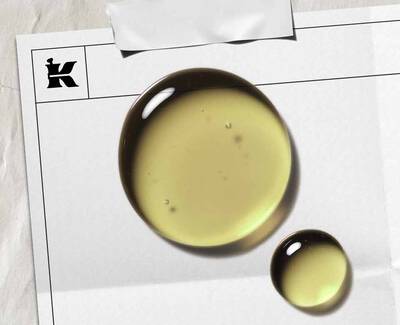 A sliced avocado revealing its seed next to a small glass bowl of golden avocado oil, all set against a rustic wooden background.