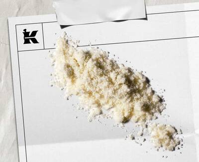 Een hoop wit poeder op een blanco vel papier met een logo in de hoek, wat een artistieke of stilistische presentatie suggereert.