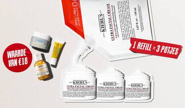 Drie reisformaat huidverzorgingsproducten van Kiehl's (de Ultra Facial Cream, de Calendula Herbal-Extract Toner en de Avocado Eye Cream) liggen verspreid op een witte, gestructureerde achtergrond. In het midden staat een rode, geverfde cirkel met de witte tekst "WAARDE VAN €18".