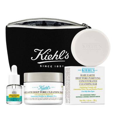 A collection of Kiehl's skincare products including a cleansing mask, purifying cleansing bar, and a serum, all displayed with a branded black zip pouch.