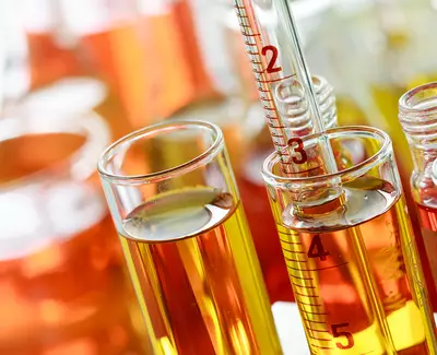 Close-up of laboratory glassware filled with colorful liquids, including test tubes and a graduated cylinder, showcasing shades of orange and yellow.