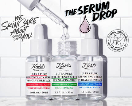 Afbeelding van drie flessen met gezichtsserums van Kiehl's op een marmeren oppervlak, met een pipet en de tekst "The Serum Drop" op een betegelde achtergrond.