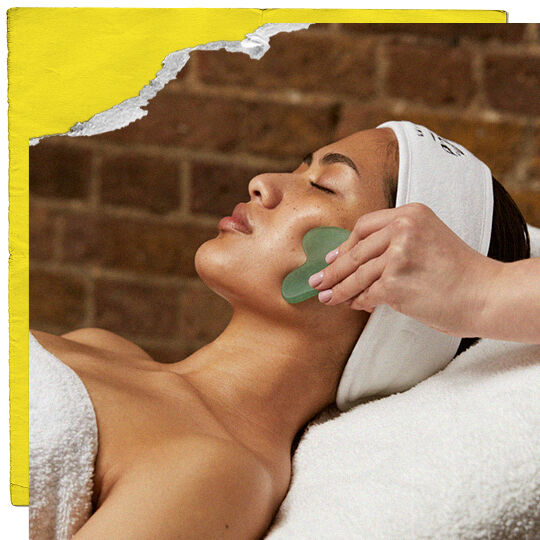 Een lachend persoon met kort donker haar en ster-oorbellen heeft een wit Kiehl's-apparaat met een gloeiende groene punt aangebracht op zijn wang door een hand. De achtergrond bevat planken en de afbeelding is omlijst met gescheurd geel papier en oranje lijnen.