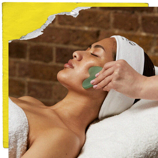 Een lachend persoon met kort donker haar en ster-oorbellen heeft een wit Kiehl's-apparaat met een gloeiende groene punt aangebracht op zijn wang door een hand. De achtergrond bevat planken en de afbeelding is omlijst met gescheurd geel papier en oranje lijnen.