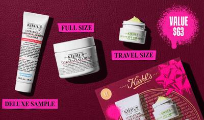 Een afbeelding, tegen een donkerrode getextureerde achtergrond, toont drie producten en een geschenkdoos. Een witte tube "KIEHL’S ULTRA FACIAL BARRIER-HYDRATING CLEANSER" is gemarkeerd met "DELUXE SAMPLE" in felroze. Een witte pot "KIEHL’S ULTRA FACIAL CREAM" is gemarkeerd met "FULL SIZE" in felroze. Een kleine witte pot "KIEHL’S CREAMY EYE TREATMENT WITH AVOCADO" met zichtbare lichtgele creme is gemarkeerd met "TRAVEL SIZE" in felroze. Rechtsonder is een rode Kiehl’s geschenkdoos zichtbaar, met dezelfde drie producten, versierd met felroze grafische verfspatten en een strikontwerp. In de rechterbovenhoek bevat een felroze verfspat de tekst "VALUE $63."