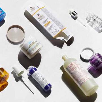 Een reeks huidverzorgingsproducten op een lichte achtergrond, waaronder flesjes, potjes en druppelaars in verschillende kleuren en vormen.