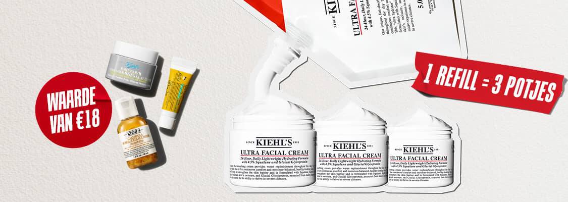 Drie reisformaat huidverzorgingsproducten van Kiehl's (de Ultra Facial Cream, de Calendula Herbal-Extract Toner en de Avocado Eye Cream) liggen verspreid op een witte, gestructureerde achtergrond. In het midden staat een rode, geverfde cirkel met de witte tekst "WAARDE VAN €18".