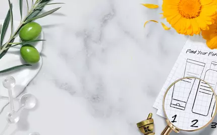 A flat lay featuring a marble background with various natural ingredients like olive branches and flowers, alongside a magnifying glass over a chart with numbered skincare formulas. A mortar and pestle are also visible, suggesting a focus on herbal remedies or skincare preparation.