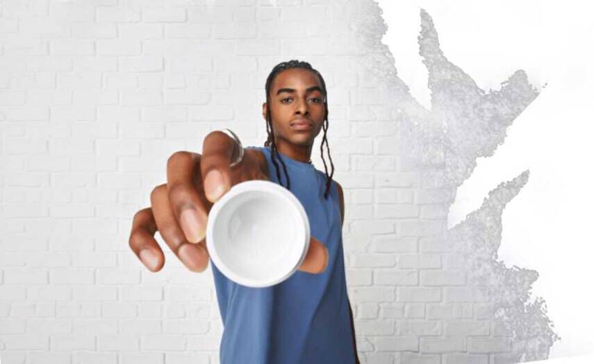 Een persoon met een blauw mouwloos shirt houdt een kleine witte kom in de richting van de camera, tegen een witte muur met textuur.