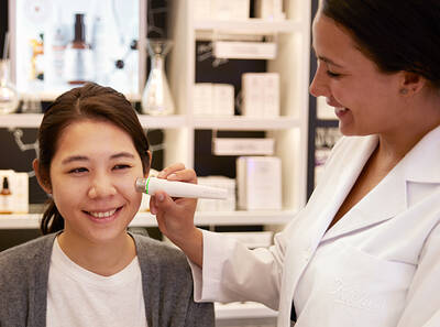A skincare professional uses an electronic device on a smiling woman's face for a treatment in a beauty store.
