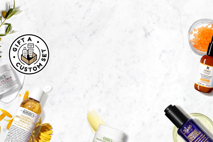 Alt-tekst: Een geschenktas van Kiehl's met verschillende huidverzorgingsproducten, waaronder een creme, een serum en een tube met een gezichtsbehandeling, op een marmeren achtergrond.