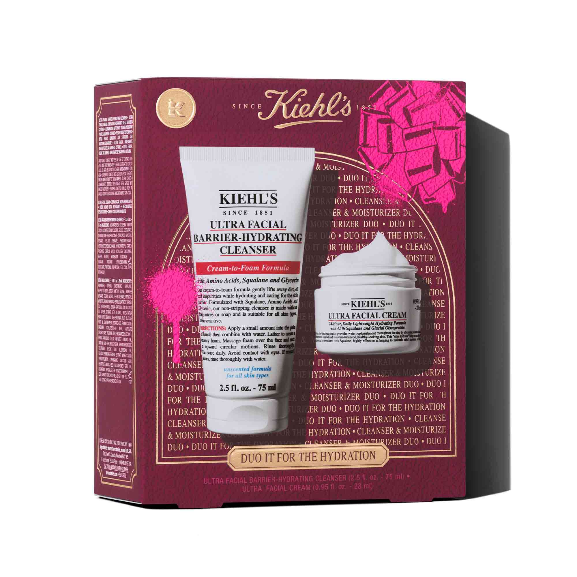 Een afbeelding toont een doos van een Kiehl's geschenkset, in donkerrood, met een roze strikafbeelding in de rechterbovenhoek en een roze verfspateffect linksonder. Op de voorkant van de doos staat "DUO IT FOR THE HYDRATION" en er staan twee producten op: een witte tube "KIEHL'S ULTRA FACIAL BARRIER-HYDRATING CLEANSER" en een witte pot "KIEHL'S ULTRA FACIAL CREAM".