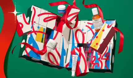 Kiehl’s feestdagen adventskalender met genummerde cadeauboxen en huidverzorgingsproducten, gestrikt met een rood lint tegen een feestelijke groene achtergrond.