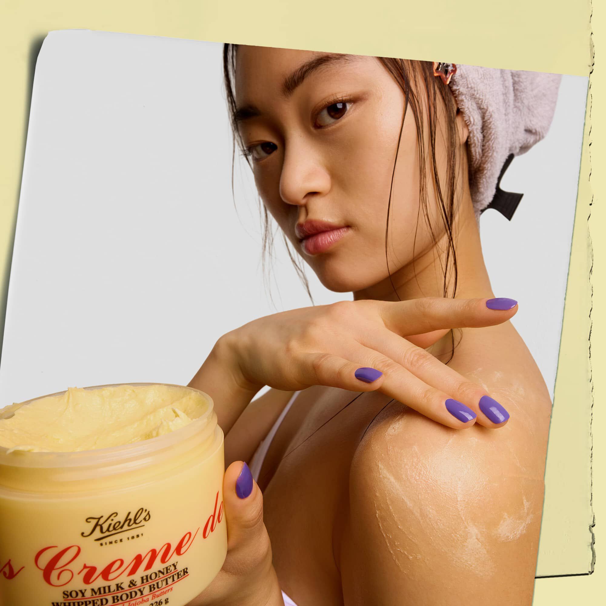Model houdt een pot vast en brengt Kiehl's Creme de Corps Whipped Butter body butter aan