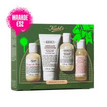 Een afbeelding met links een groene en gouden Kiehl's geschenkdoos met vier producten. Rechts van de doos staan dezelfde vier producten buiten de doos: een flesje "KIEHL'S CREME DE CORPS", een tube "KIEHL'S AMINO ACID CONDITIONER", een flesje "KIEHL'S AMINO ACID SHAMPOO" en een flesje "KIEHL'S GENTLY EXFOLIATING BODY SCRUB GRAPEFRUIT". De doos is versierd met felgroene grafische accenten en heeft onderaan de tekst "OH SOFT & SUDSY".