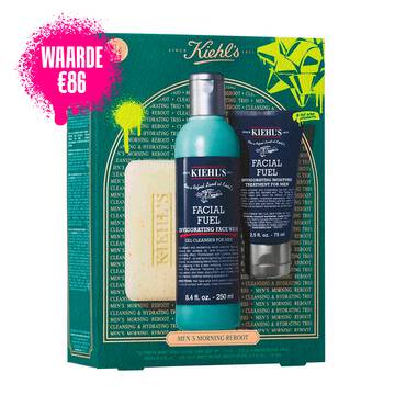 Een afbeelding van een donker groenblauwe geschenkdoos van Kiehl's met witte en gouden accenten aan de linkerkant. De doos bevat drie producten. Rechts van de doos staan dezelfde drie producten buiten de doos: een reep "KIEHL'S 'ULTIMATE MAN' BODY SCRUB SOAP", een blauwe fles "KIEHL'S FACIAL FUEL ENERGIZING FACE WASH" en een donkerblauwe tube "KIEHL'S FACIAL FUEL MOISTURIZER". De doos is versierd met felgroene grafische verfspatten en een strikontwerp en bevat de tekst "MEN'S MORNING REBOOT" aan de onderkant.
